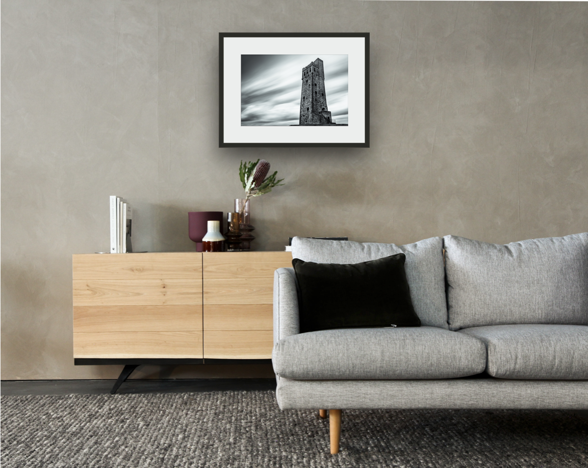 Framed and mounted photograph of the Victoria Tower on Castle Hill in Huddersfield above a sofa and cupboard.