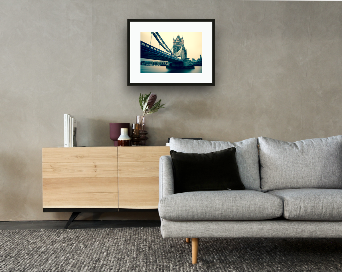 Framed and mounted photograph of Tower Bridge on the river Thames in central London hanging on a wall above a sofa and cupboard